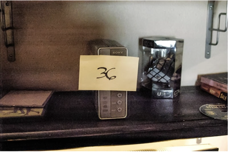 FBI search photo — bookshelf with Item 36, surrounded by added props (IMAGE TO BE ADDED)